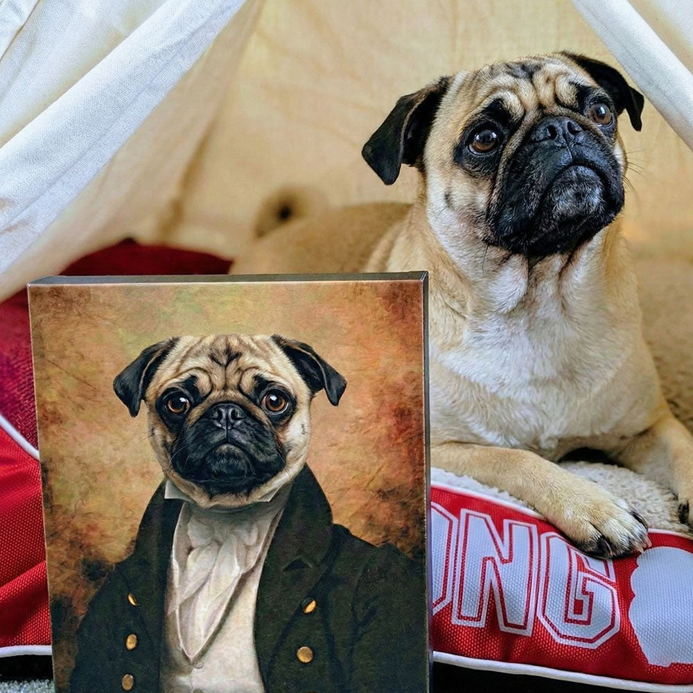 Pug dog sitting next to a portrait of a pug in formal attire inside a tent.