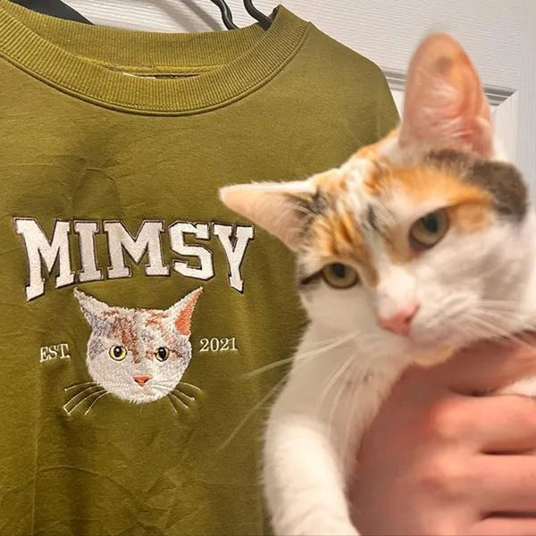 A custom sweatshirt featuring an embroidered pet portrait and personalized text in a varsity style font.
