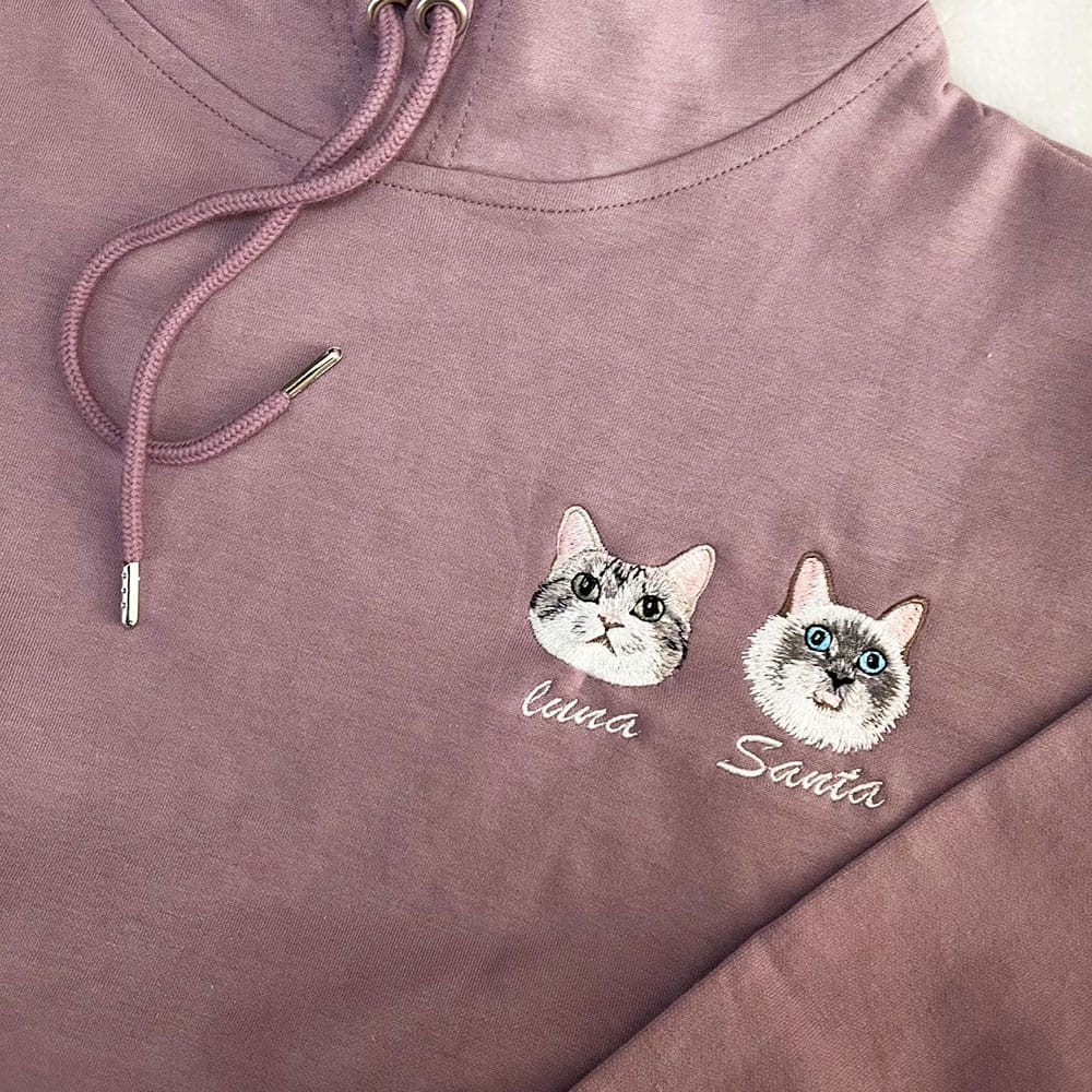Purple hoodie with embroidered cat faces and names on a white background