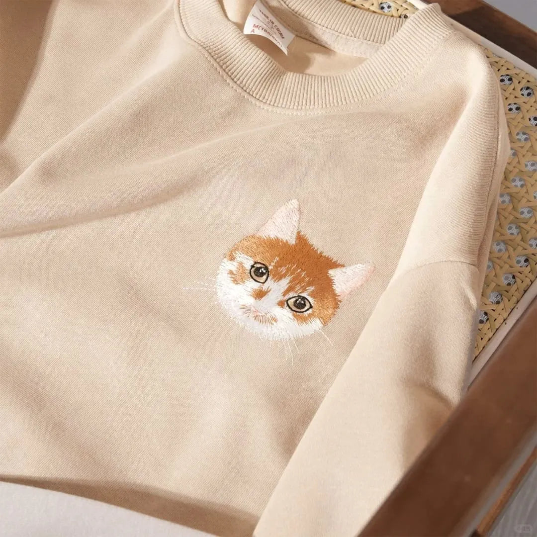 A beige sweatshirt featuring a custom embroidered pet portrait.