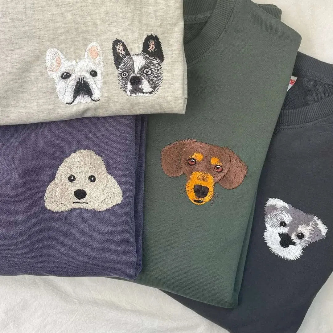 A collection of custom embroidered pet portrait sweatshirts in various colors, showcasing different dog breeds.