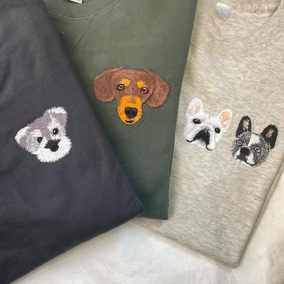 Three sweatshirts with embroidered dog faces on a white surface