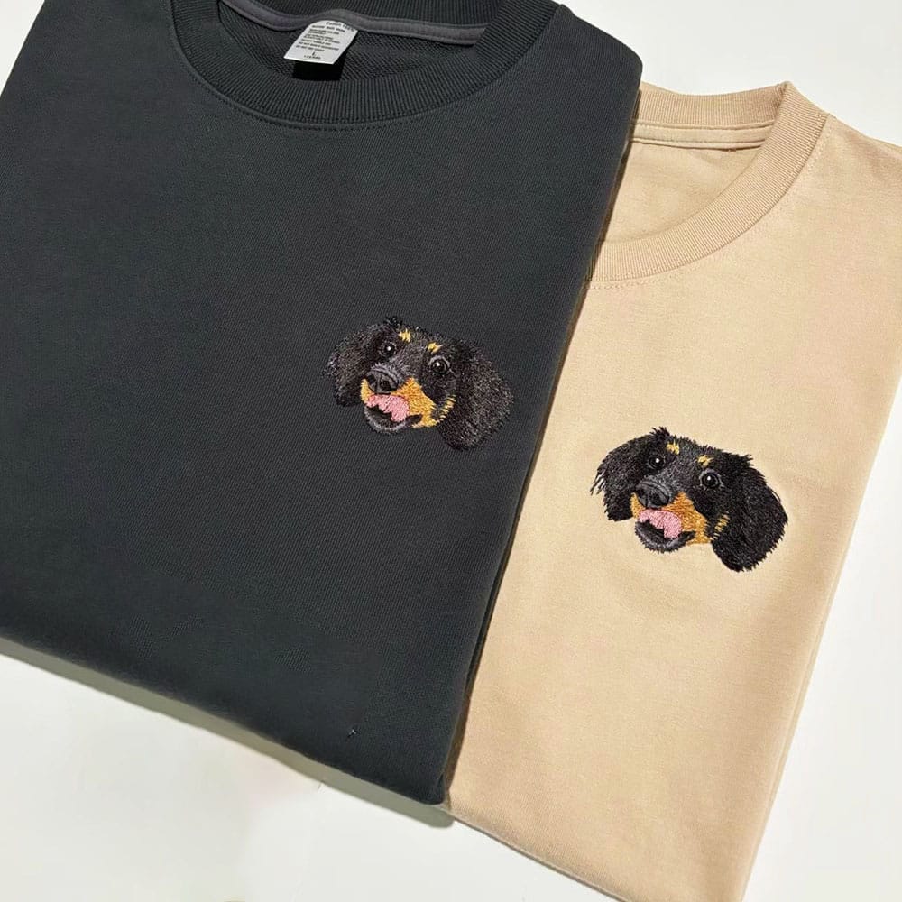 Black and beige sweatshirts with embroidered dachshund faces on a white background