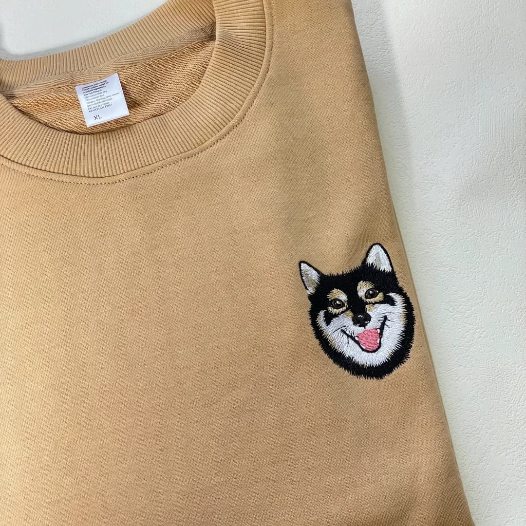 Beige sweatshirt with an embroidered dog face on a white background