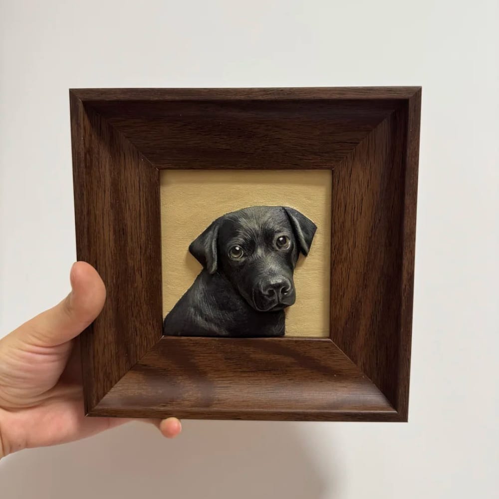 A custom pet portrait wood carving of a black dog puppy, held in a dark wood frame.