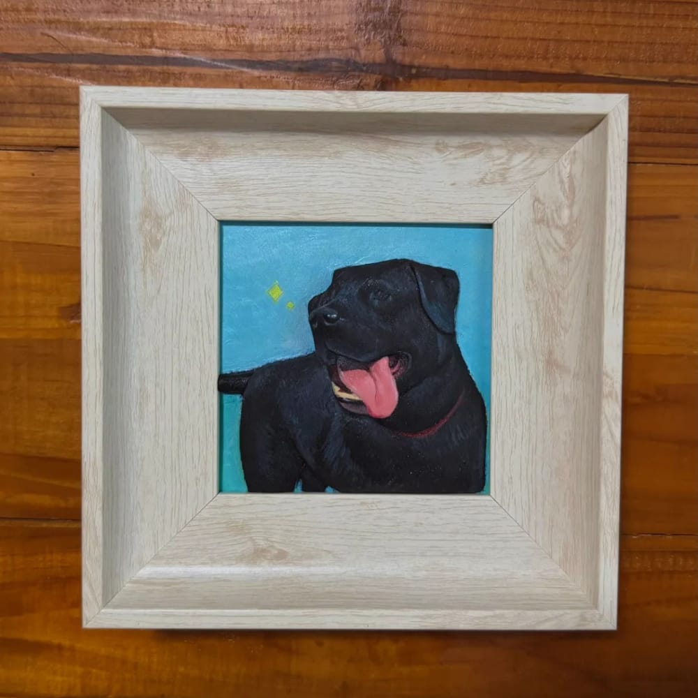 A custom pet portrait wood carving of a black dog with a blue background, set in a light wood frame.