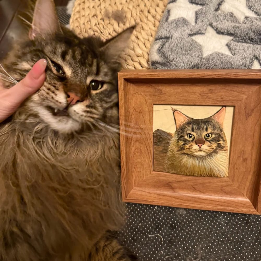 A custom pet portrait wood carving of a long-haired tabby cat, displayed in a wood frame.