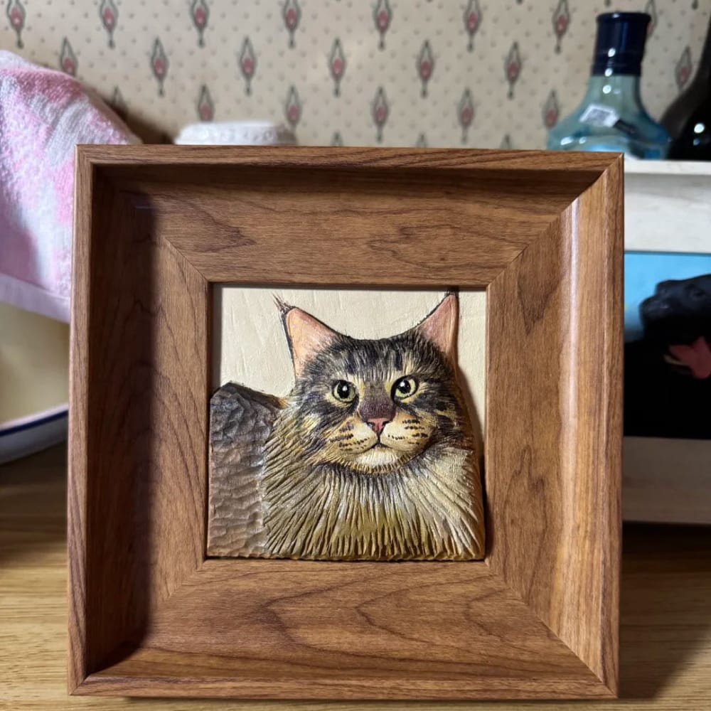 A custom pet portrait wood carving of a long-haired tabby cat, displayed in a wood frame.