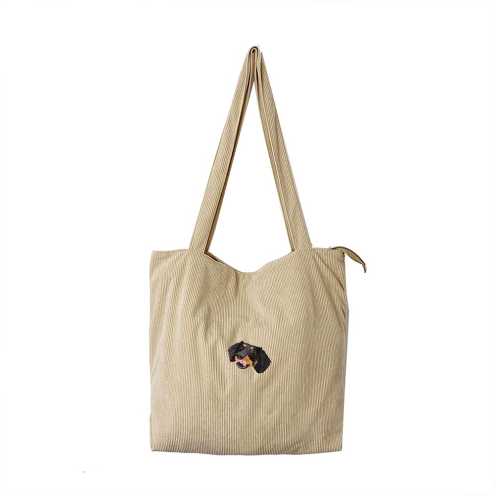 A beige corduroy bag featuring a custom embroidered pet portrait.