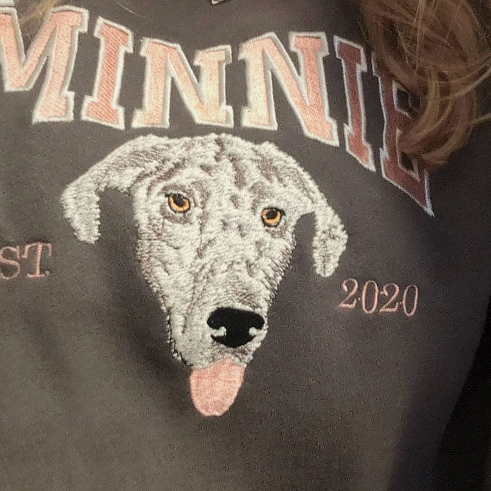 A brown sweatshirt featuring a custom embroidered dog portrait with personalized text in a varsity style font.