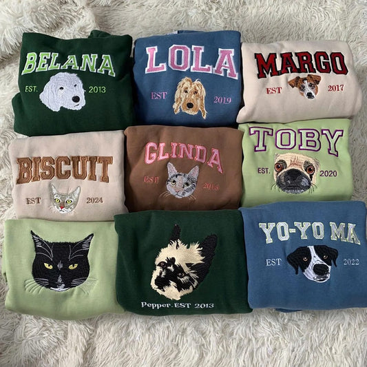 Collection of folded sweatshirts with embroidered names and animal illustrations on a textured surface.